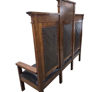 May include: A high-backed wooden bench featuring a dark brown oak frame with a prominent grain pattern. The backrest and seat are upholstered in dark leather, secured with metal nailhead trim along the edges. The bench has flat armrests.