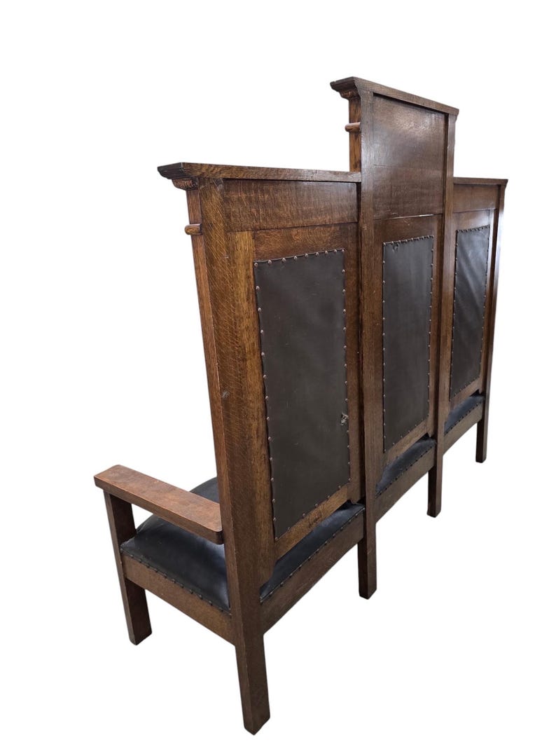 May include: A high-backed wooden bench featuring a dark brown oak frame with a prominent grain pattern. The backrest and seat are upholstered in dark leather, secured with metal nailhead trim along the edges. The bench has flat armrests.