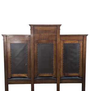 May include: A wooden sideboard featuring three vertical panels with dark brown leather-like inserts secured by metal studs. The piece has a raised central section, a natural wood grain finish, and a rectangular frame supported by four sturdy legs.