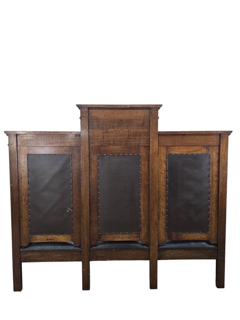 May include: A wooden sideboard featuring three vertical panels with dark brown leather-like inserts secured by metal studs. The piece has a raised central section, a natural wood grain finish, and a rectangular frame supported by four sturdy legs.