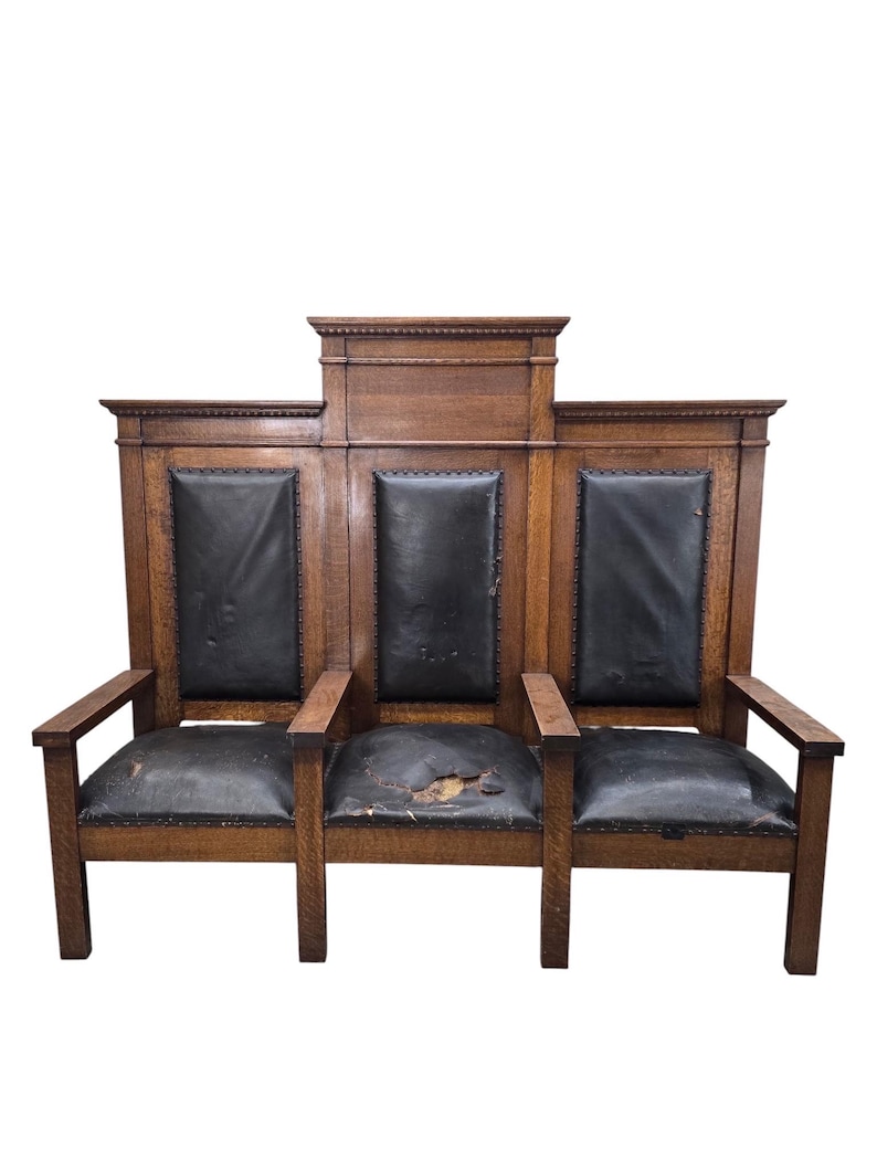 May include: A three-seat wooden bench featuring a high backrest with three distinct sections. The frame is constructed from brown wood with a visible grain. Each seat and back panel is upholstered in black material, showing signs of wear.