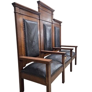 May include: A tall, three-seat wooden bench featuring a dark brown oak frame and black leather upholstery on the backrests and seats. The high back panels are segmented with decorative molding, and the seats are secured with metal nailhead trim.