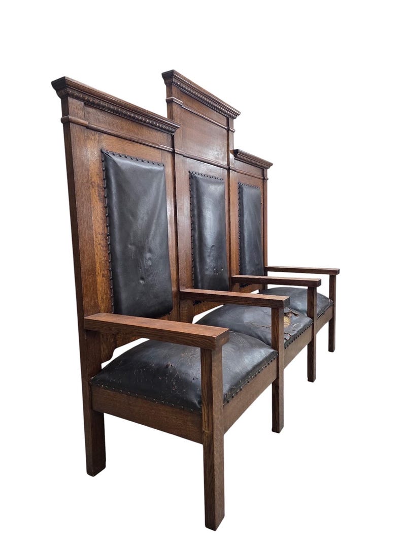 May include: A tall, three-seat wooden bench featuring a dark brown oak frame and black leather upholstery on the backrests and seats. The high back panels are segmented with decorative molding, and the seats are secured with metal nailhead trim.
