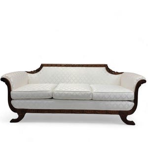 May include: A three-cushion sofa with a white patterned fabric and dark wood frame. The sofa has curved arms and decorative carvings along the base and back. The overall design is classic and elegant.