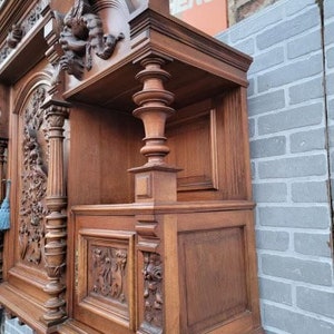 May include: A large, intricately carved wooden cabinet with a dark brown finish. The cabinet has multiple shelves and drawers, and is decorated with ornate carvings of flowers, leaves, and other designs. The cabinet is a beautiful example of antique furniture.