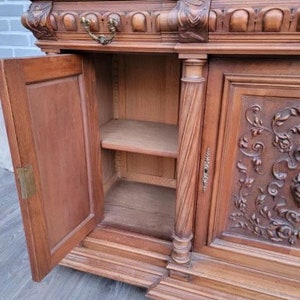 May include: A large, antique wooden cabinet with intricate carvings and a marble top. The cabinet has two doors, one of which is open, revealing shelves inside. The cabinet is made of dark wood and has a rich, warm patina.