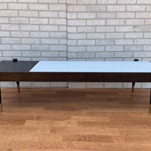 Może przedstawiać: Stolik kawowy w stylu mid-century modern z ciemnym drewnianym blatem i białym wkładką laminowaną. Stolik ma cztery zwężające się nogi ze złotymi akcentami.