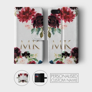 K&ouml;nnte beinhalten: Eine wei&szlig;e Handyh&uuml;lle mit einem Blumendesign in den Farben Burgunderrot, Rosa und Gr&uuml;n. Die H&uuml;lle hat eine Klappe, die den Bildschirm des Handys bedeckt, und ein goldenes Monogramm "MK" auf der Vorderseite.