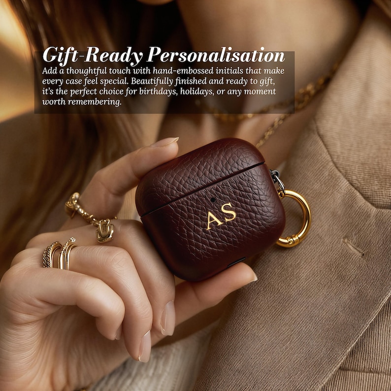 May include: A burgundy leather AirPod case with gold-colored hardware and the initials "AS" embossed on the front. The case has a textured surface and is held by a person. The text "Gift-Ready Personalisation" is visible in the background.