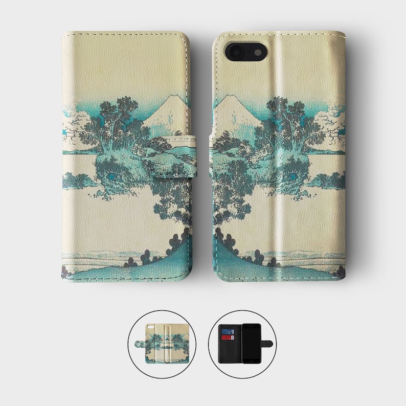 May include: A beige leather phone case with a Japanese-inspired design featuring a mountain and trees in blue and green hues. The case has a flap that folds over the phone screen and a slot for cards.
