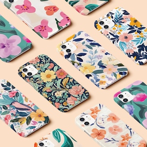 May include: A selection of phone cases with floral patterns. The cases display designs with pink, orange, yellow, and blue flowers on white or dark backgrounds. The cases are arranged on a light peach surface.