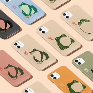 May include: A set of ten phone cases featuring a green frog illustration with a red stamp that says "蛙" in Japanese. The cases are in various colors, including beige, light blue, pink, orange, and green.