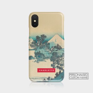 May include: A beige iPhone case with a Japanese-style print of a mountain and trees. The case has a red rectangle with the name "CHARLOTTE" printed on it. The text "PERSONALISED CUSTOM NAME" is printed in black on a white rectangle in the lower right corner.
