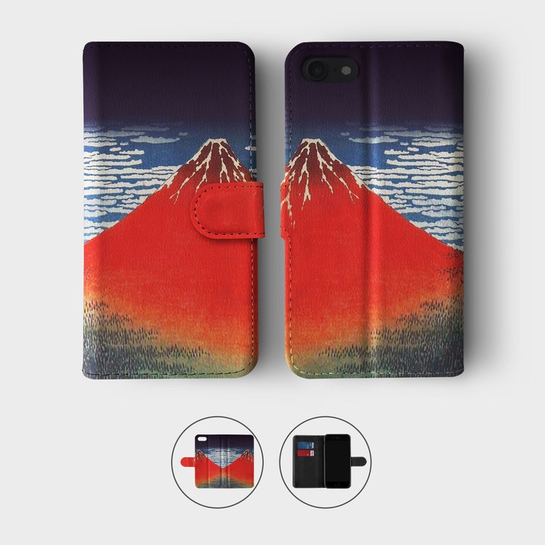 May include: A black leather phone case with a red and white image of Mount Fuji. The case has a flap that folds over the front of the phone and a slot for cards.