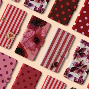 May include: A collection of rectangular phone cases featuring various patterns including red and white stripes, red and pink polka dots, and floral prints with red and purple flowers. One case displays a single cherry and another has heart stamps.