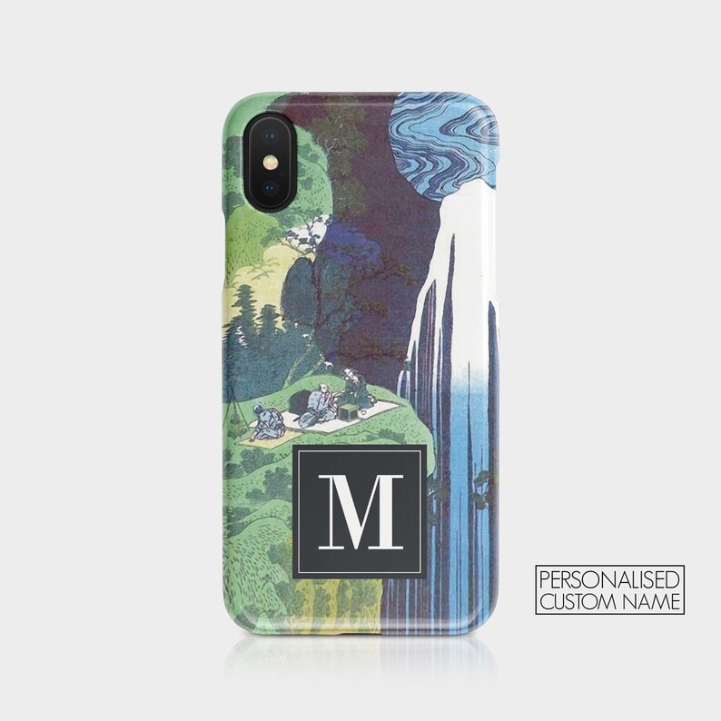 May include: A phone case with a blue and green Japanese-inspired design. The case features a waterfall and a mountain scene with a black square with a white letter "M" in the center.