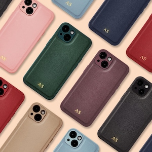 May include: Assortment of ten phone cases in various colors and textures. The cases are all for the same model phone and have a flap that covers the screen. The cases are arranged in a circle on a light brown background. The cases are made of leather and have a subtle texture. The cases are all personalized with the initials "AS".