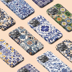 Puede incluir: Una colección de fundas para teléfonos con varios patrones decorativos. Las fundas presentan diseños florales, geométricos e inspirados en azulejos en tonos azules, blancos, amarillos y naranjas. Las fundas están dispuestas sobre una superficie beige claro.