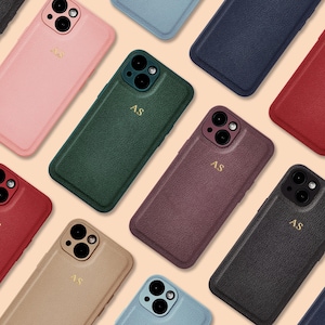 May include: A selection of leather phone cases in shades like pink, green, and black. Each case has a textured finish and the gold initials "AS". These cases are designed to fit a smartphone, offering protection and style.