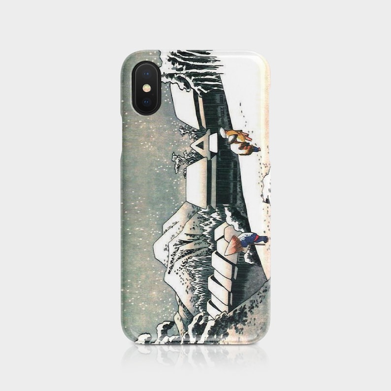 May include: A phone case featuring a Japanese woodblock print of a waterfall and figures. The design includes shades of white, gray, and brown, with a detailed depiction of the landscape and figures. The case is made of a glossy material.