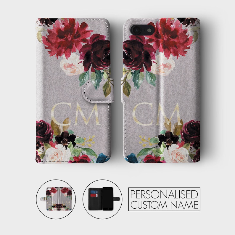 K&ouml;nnte beinhalten: Eine graue Handyh&uuml;lle mit einem Blumendesign mit burgunderfarbenen, rosa und wei&szlig;en Blumen. Die H&uuml;lle hat eine Klappe, die &uuml;ber das Telefon klappt und die Initialen "CM" in goldener Schrift tr&auml;gt.