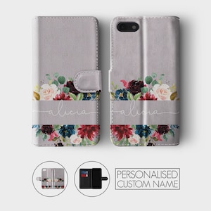 K&ouml;nnte beinhalten: Eine graue Leder-Handyh&uuml;lle mit einem Blumendesign und dem Namen "Alicia" in wei&szlig;er Schrift. Die H&uuml;lle hat eine Klappe, die sich &uuml;ber den Bildschirm des Handys klappen l&auml;sst.