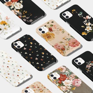 May include: A selection of iPhone cases showcasing floral patterns. The cases come in a range of colours and designs, including black, white, beige, and grey. Some cases feature small floral prints, while others have larger, more intricate floral designs.