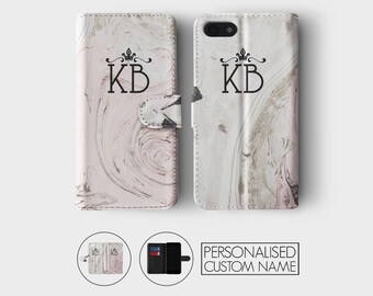 May include: A pink and white marble patterned phone case with a black crown and the initials "KB" in a black font. The case is a wallet style with a flap that folds over the phone.