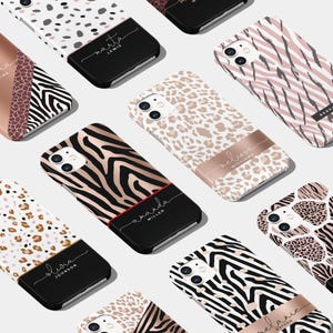 Könnte beinhalten: Eine Sammlung von Handyhüllen mit verschiedenen Tiermuster-Designs. Die Hüllen sind schwarz mit einem goldenen Akzent und tragen einen Vor- und Nachnamen in einer kursiv geschriebenen Schrift. Die Designs umfassen Zebra-, Leopard- und Gepardenmuster.