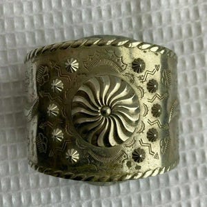 Pode incluir: Um bracelete de prata com um design detalhado de padrões em espiral e formas geométricas. O bracelete é feito de metal e tem um acabamento polido.