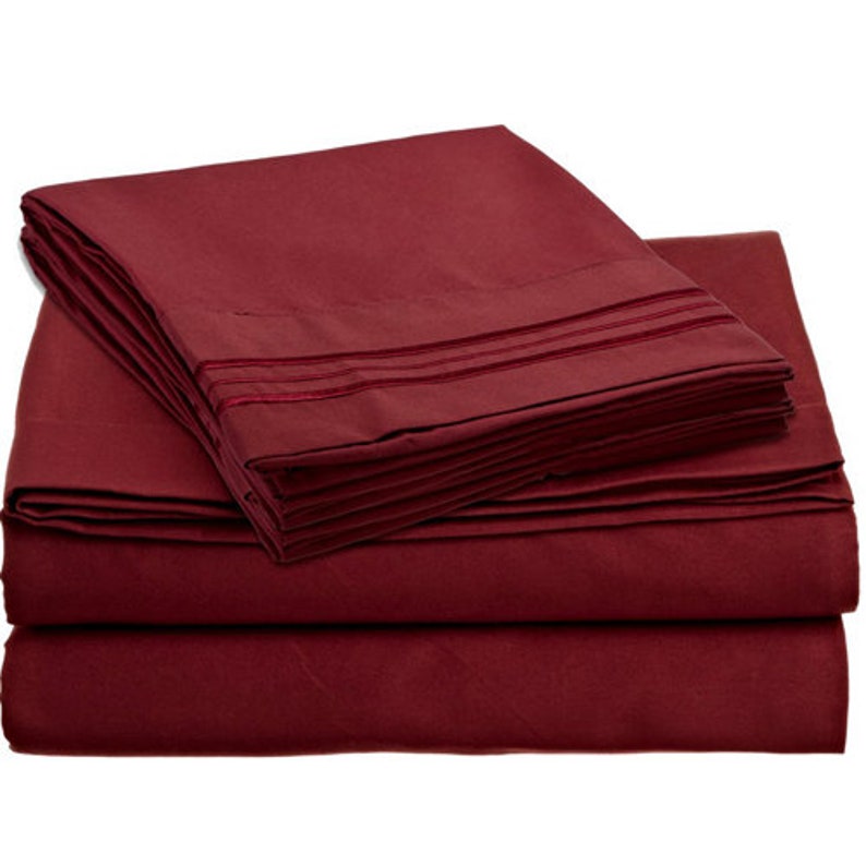 May include: A set of burgundy bed sheets with a decorative trim. The sheets are folded and stacked on top of each other.