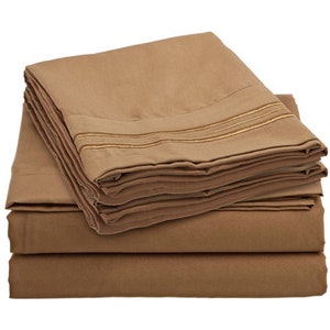 May include: A stack of brown bed sheets with gold trim. The sheets are folded neatly and are ready to be used.