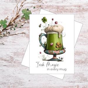 May include: A greeting card featuring a whimsical illustration of a green beer mug with a frothy top, shamrocks, and floral accents. The text "Irish Magic in every mug" is written in elegant script. The card is set against a white background.