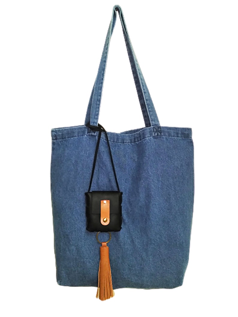 May include: A blue denim tote bag with a black leather pouch and a brown tassel attached to a gold key ring.