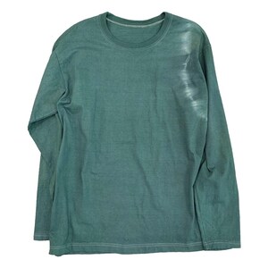 May include: A long-sleeved, crew neck shirt in a muted teal green color. The shirt has a slightly faded appearance, with a lighter, almost white, vertical streak on the right side. The fabric appears soft and comfortable.