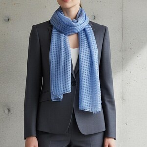 May include: A light blue scarf with a checkered pattern is draped over a dark gray blazer. The scarf is made of a lightweight fabric and adds a pop of color to the outfit. The blazer is part of a suit, suggesting a professional or formal style.