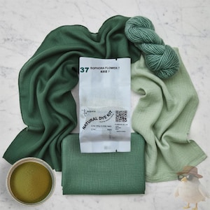 May include: An assortment of green fabric, yarn, and dye kit components. The kit includes a packet labeled "Sophora Flower 7" and a small container of green powder. Various shades of green textiles are arranged around the kit.