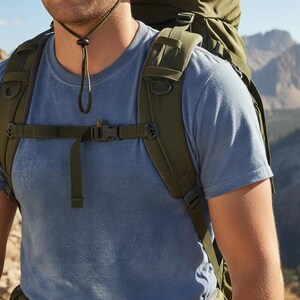 May include: A person wearing a blue t-shirt and a green hiking backpack with adjustable straps and buckles. The backpack has a large main compartment and multiple smaller pockets. The background shows a mountain range.