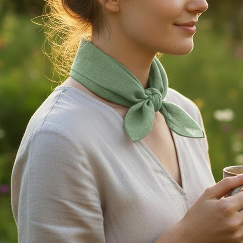 May include: A light green neck scarf tied in a knot. The scarf is made of a soft fabric and is worn around the neck. The person is wearing a light gray shirt.