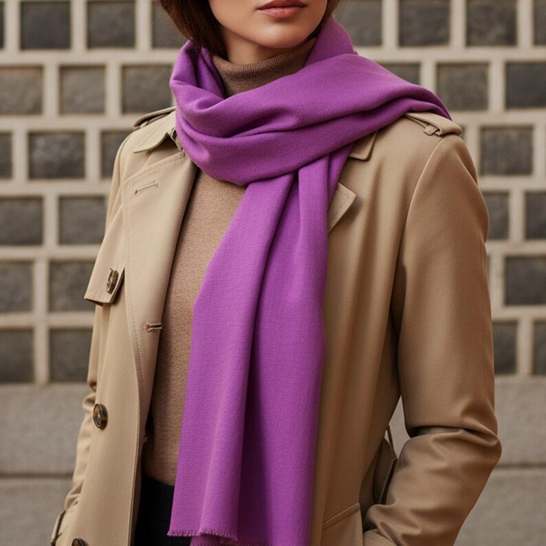 May include: A vibrant purple scarf draped over a tan trench coat. The scarf is made of a soft material and contrasts with the neutral tones of the coat and a brown turtleneck. The scarf adds a pop of color to the outfit.