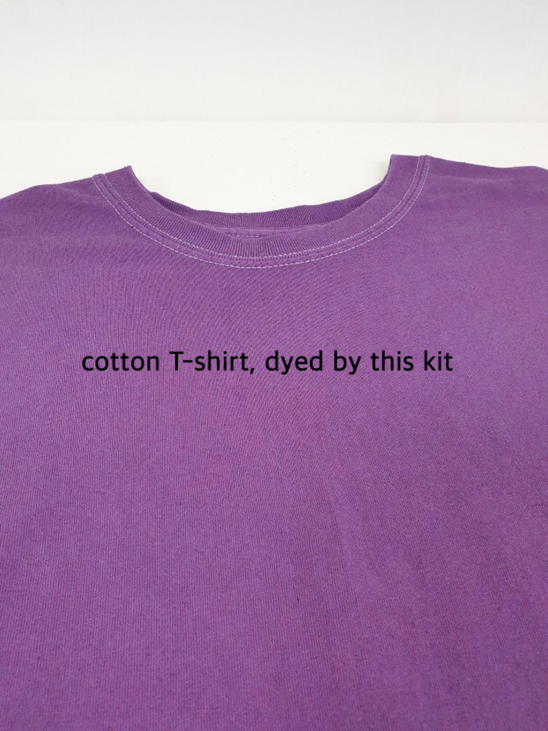 May include: A close-up of a purple cotton T-shirt. The shirt has a crew neck with white stitching. The text "cotton T-shirt, dyed by this kit" is printed on the shirt.