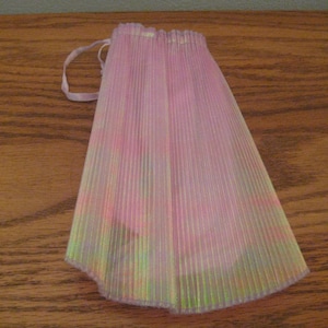 May include: A light pink, semi-sheer, pleated fabric skirt with a subtle iridescent finish. The garment features a gathered waistline with a thin, matching pink ribbon drawstring tie extending from the side, creating a soft, vertical texture.