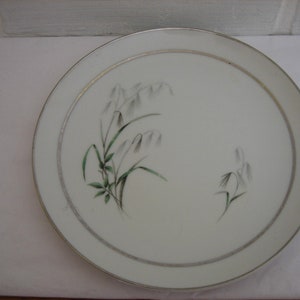 Puede incluir: Un plato de cerámica blanco con un borde dorado y un delicado diseño floral con hojas verdes y flores blancas.