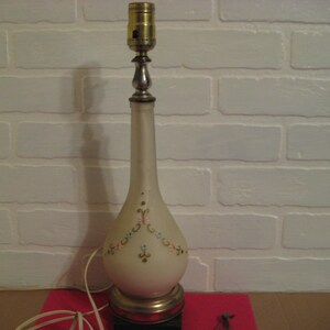 Peut inclure: Une lampe de table en céramique blanche avec un motif floral. La lampe a une base argentée et une douille dorée.