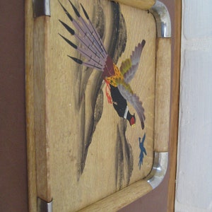 May include: Wooden serving tray featuring a painted pheasant design. The tray has a light wood frame with metal corner accents. The pheasant is depicted in flight with a mix of colours including purple, yellow, and black.