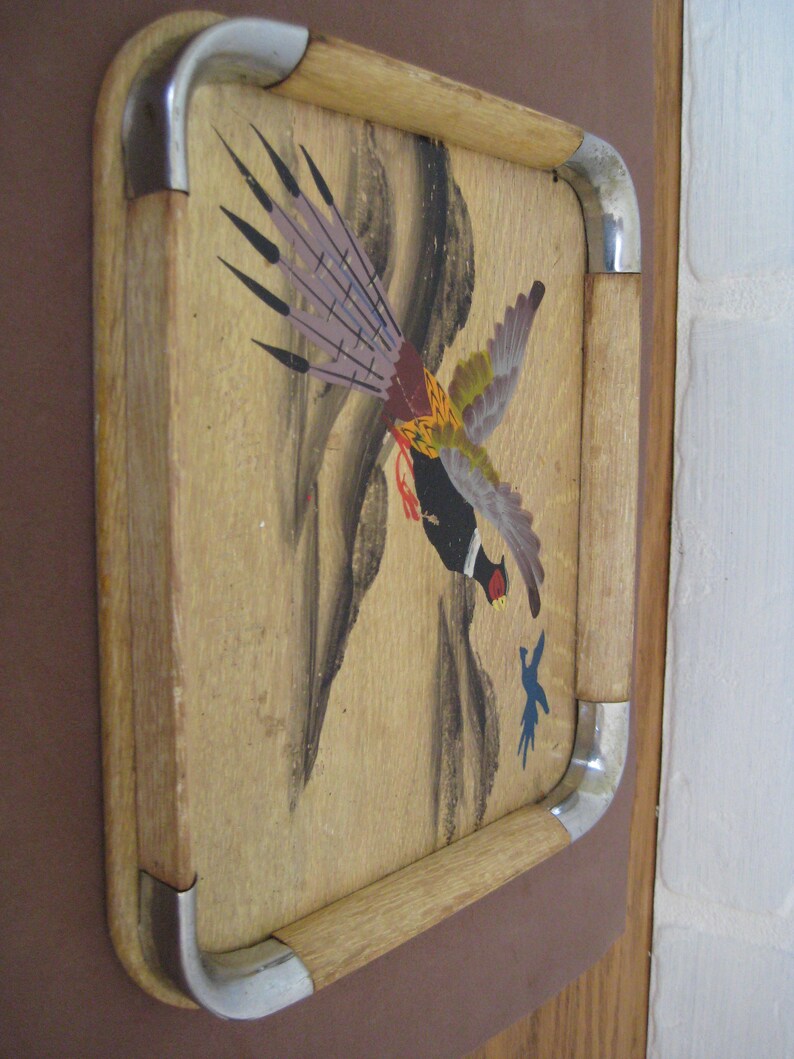 May include: Wooden serving tray featuring a painted pheasant design. The tray has a light wood frame with metal corner accents. The pheasant is depicted in flight with a mix of colours including purple, yellow, and black.