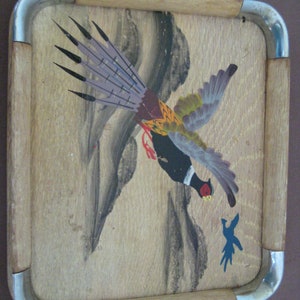 May include: A rectangular wooden tray featuring a painted pheasant design. The bird is shown in flight with a black head, red details, and colourful wings. The tray has a light wood frame with metal corner accents.