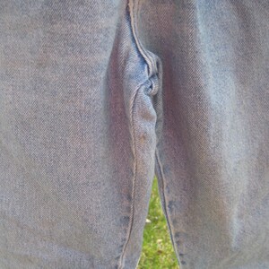 Op de afbeelding: Close-up van lichtblauwe spijkerbroek. De jeans vertoont tekenen van slijtage, met zichtbare vervaging en lichte verkleuring. De textuur van de stof is duidelijk zichtbaar en benadrukt de denimweving.