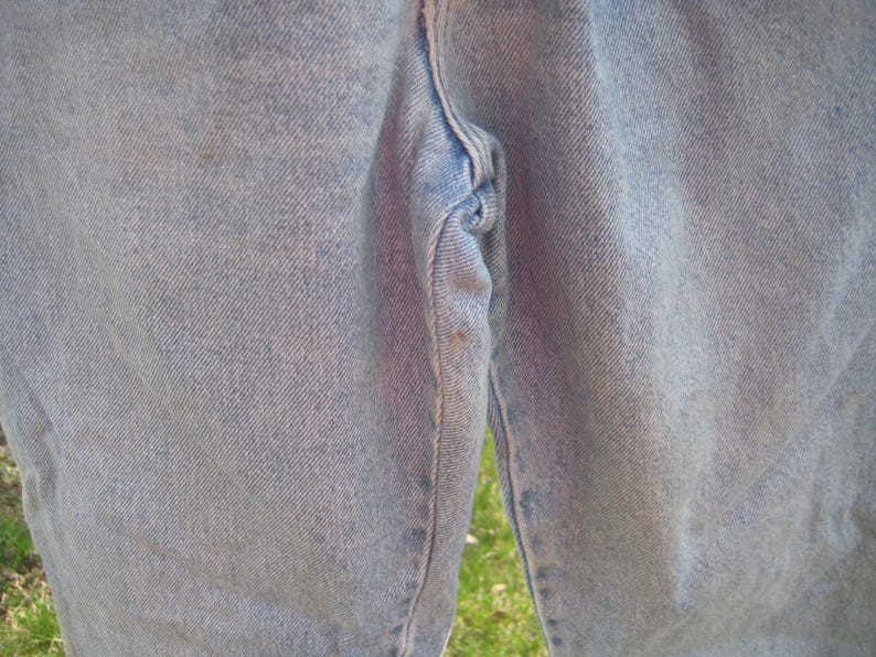 Op de afbeelding: Close-up van lichtblauwe spijkerbroek. De jeans vertoont tekenen van slijtage, met zichtbare vervaging en lichte verkleuring. De textuur van de stof is duidelijk zichtbaar en benadrukt de denimweving.