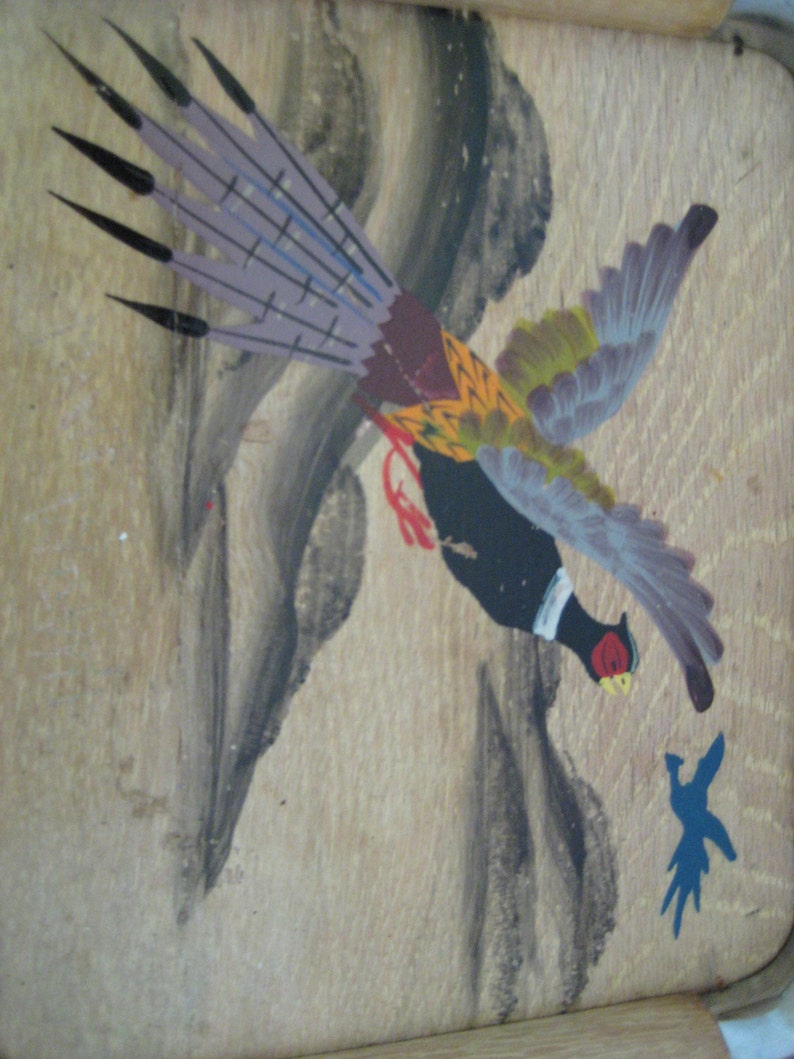May include: Hand-painted artwork of a pheasant in flight, featuring a black body, red accents, and a detailed tail with purple and black feathers. The bird is set against a light brown wooden background with abstract grey and blue painted elements.